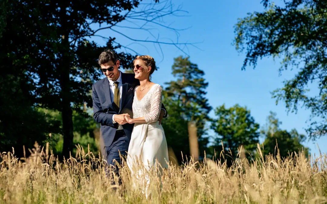 Couple de mariés se promènent dans des hautes herbes au soleil dans un environnement boisé